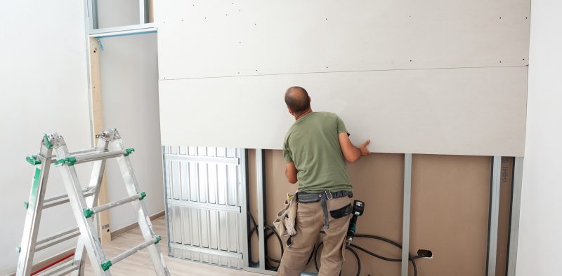Worker building plasterboard wall. Working with cutting tools, fixing and measuring for drywall.